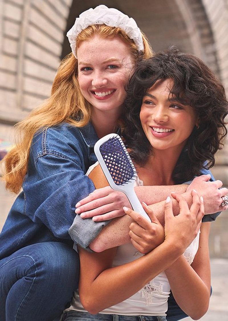 Two friends holding a hair brush from the Lee x Goody Collab. 