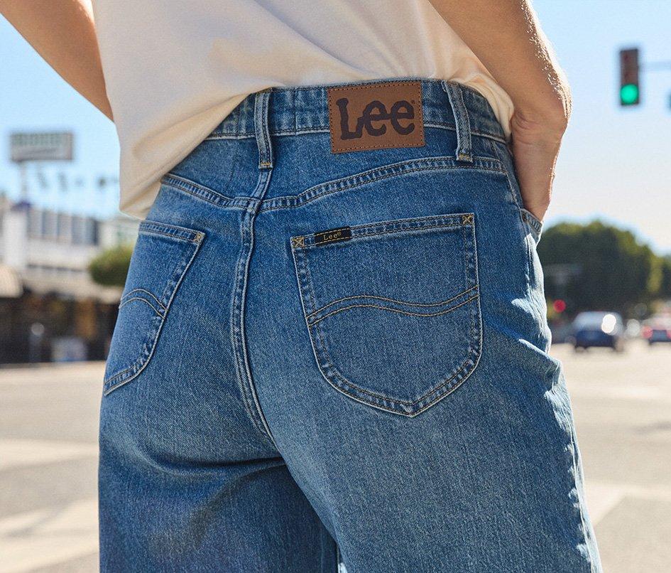 Woman standing on city street her back to the camera wearing high-waisted Lee Jeans. 