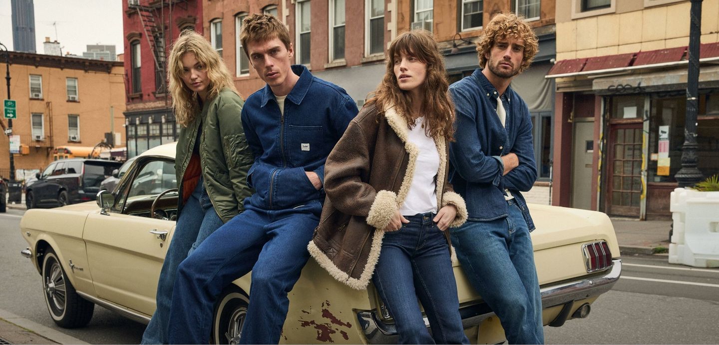 Vier junge Leute in stylischen Jeans sitzen für die Winterkampagne von Lee auf der Motorhaube eines Autos und genießen den Herbsttag.