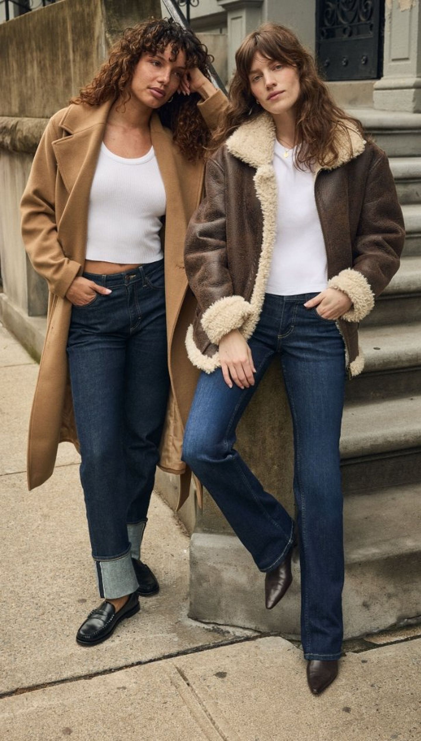 Two women in fall outfits pose on a city sidewalk—one in a camel coat, the other in a shearling jacket.