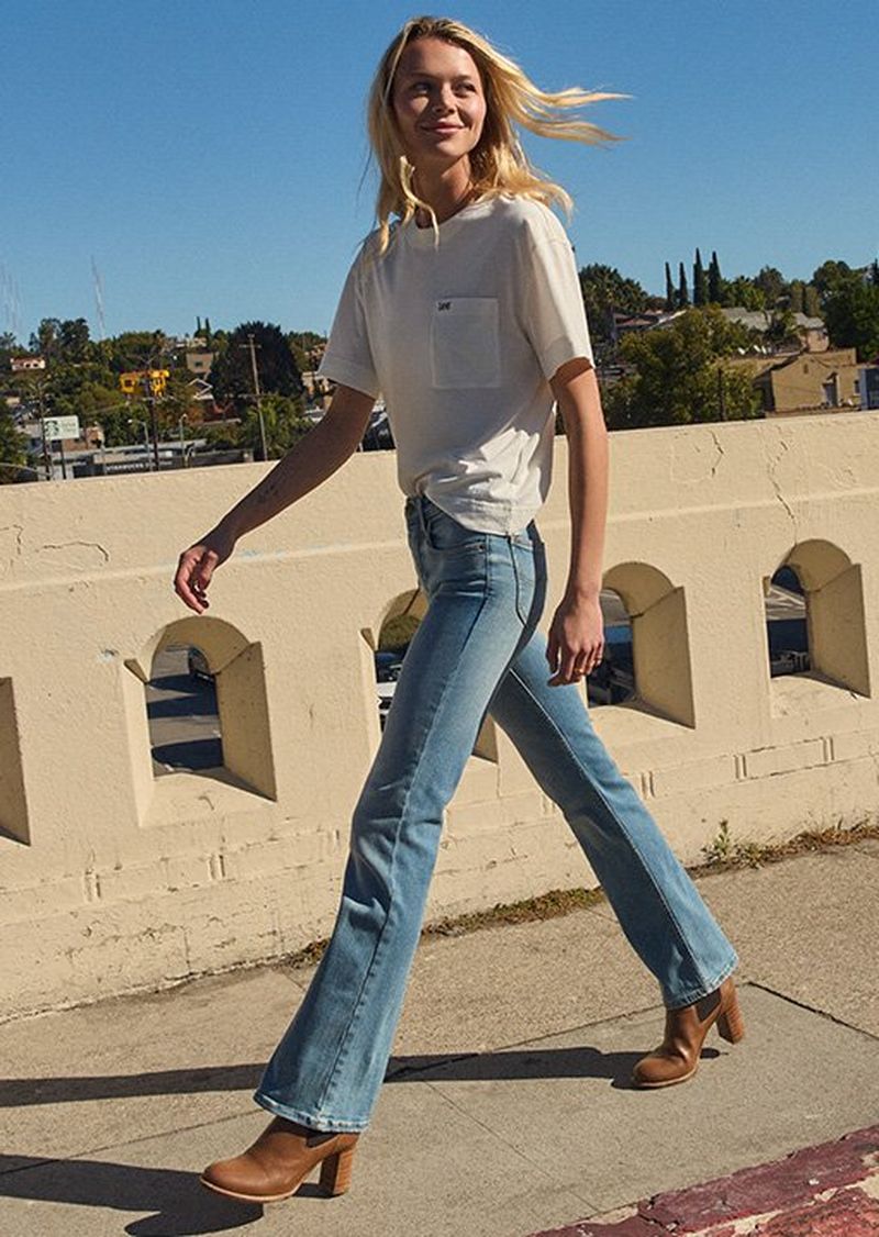 Woman walking across a bridge in the city wearing Lee light wash denim. 